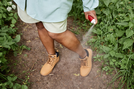 High angle closeup of black woman spaying legs with bug repellent while travelling in natureの写真素材