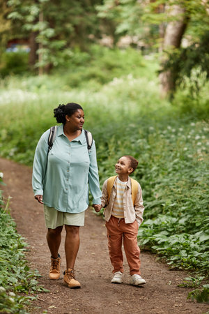 Vertical portrait of black mother and daughter walking on nature trail together holding handsの写真素材
