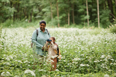 Portrait of black mother and daughter hiking in nature and looking in binoculars, copy spaceの写真素材