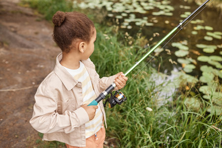 High angle portrait of black little girl fishing by forest lake and enjoying nature, copy spaceの写真素材