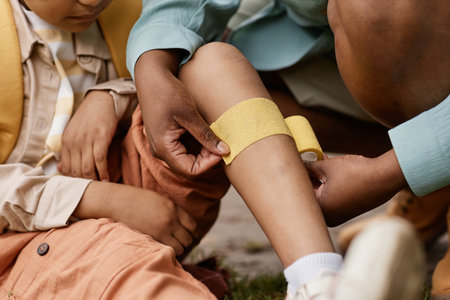 Close up of caring mother putting bandage on childs knee outdoorsの写真素材