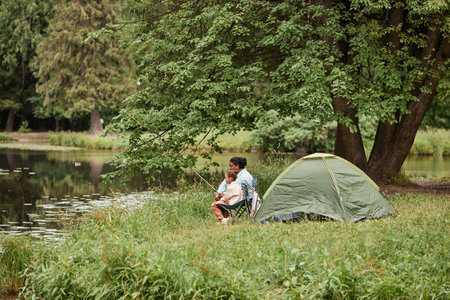Wide angle view at mother and daughter camping together outdoors and fishing, copy spaceの写真素材