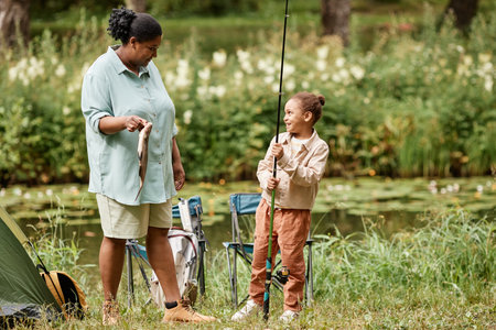 Full length portrait of happy mother and daughter fishing together during camping in natureの写真素材
