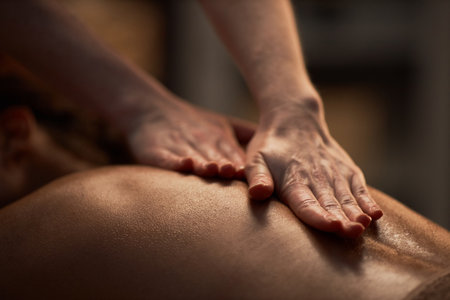 Hands of masseuse applying oil on back of young womanの写真素材