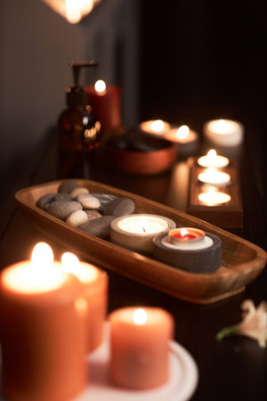 Wooden bowl with stones and burning candles in massage room in spa salonの写真素材
