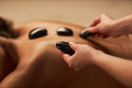 Spa therapist putting hot stones on back of young woman