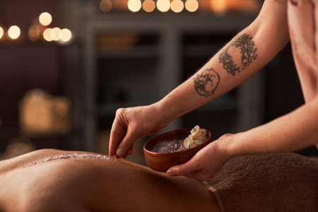 Spa therapist putting sea salt along spine of female clientの写真素材