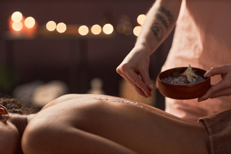 Spa therapist putting infused sea salt along spine of young womanの写真素材