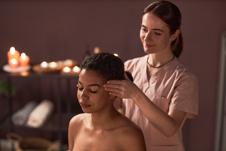 Smiling woman massaging temples of relaxed female clientの写真素材