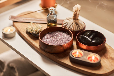 Wooden bowl with scented bath salt next to burning candles and incense stickの写真素材