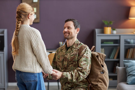 Portrait of loving father wearing military uniform holding hands with teen daughterの写真素材