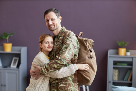 Side view portrait of man wearing military uniform embracing daughter and looking at cameraの写真素材