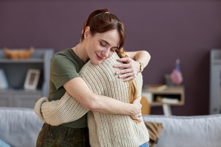 Portrait of woman serving in military embracing daughter at home and smilingの写真素材