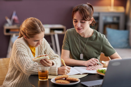 Portrait of military mother helping teen daughter with homework and eating lunchの写真素材