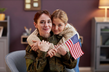Portrait of military mother with daughter embracing and looking at camera at homeの写真素材