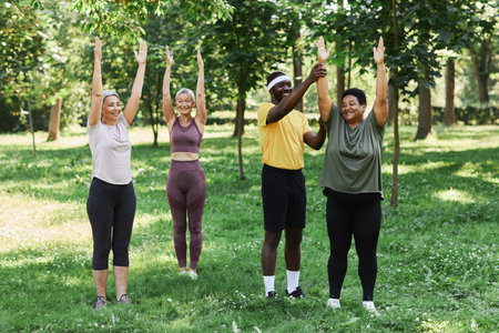 Diverse group of seniors working out outdoors in green park with coach and smiling happilyの写真素材