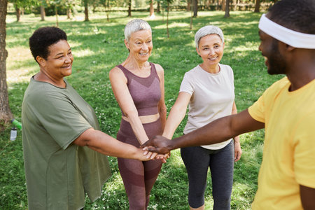 Group of active senior women stacking hands with trainer after enjoying outdoor workout in parkの写真素材