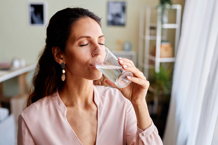 Portrait of beautiful adult woman drinking water in morning while starting day at home