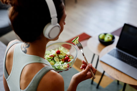 High angle view of sportive young woman eating fresh salad while enjoying healthy lifestyle and organic eating at homeの写真素材