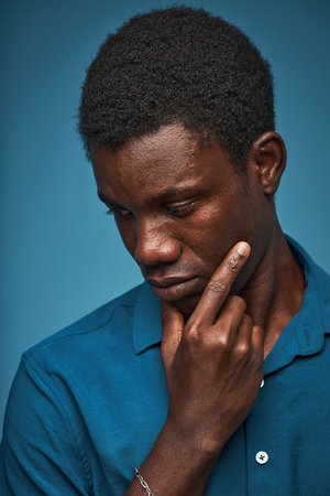 Vertical closeup portrait of young black man thinking against blue background