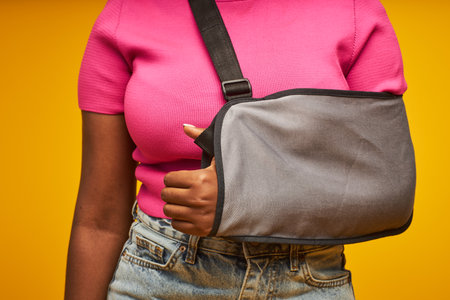 Minimal closeup of unrecognizable black woman with arm sling against yellow background