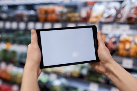 Close up of female hands holding tablet with white screen mockup in supermarket, copy spaceの写真素材