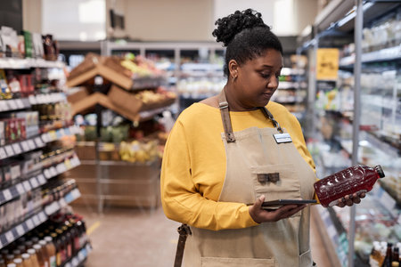 Waist up portrait of young black woman working in supermarket and doing stock inventoryの写真素材