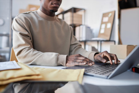 Close-up of young male manager of storage room typing on laptop keyboard while sitting by workplace and checking new online ordersの写真素材