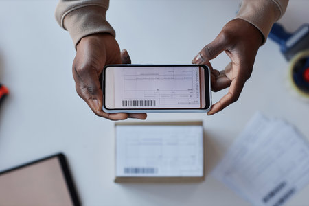 Above view of hands of young African American man with smartphone over packed box taking photo of form with address of receiverの写真素材