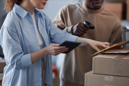 Young female manager of post office or storage room with tablet pointing at envelope with letter while checking number of packet or addressの写真素材