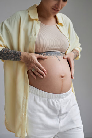 Close up of tattooed pregnant woman in minimal studio setting with focus on bellyの写真素材