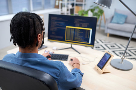 Back view at black young man writing code while studying computer programming at home, copy spaceの写真素材
