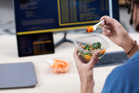 Closeup of unrecognizable man eating takeout lunch at workplace while writing codeの写真素材