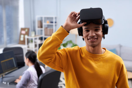 Waist up portrait of black young man using VR in IT development office and smiling at camera, copy spaceの写真素材