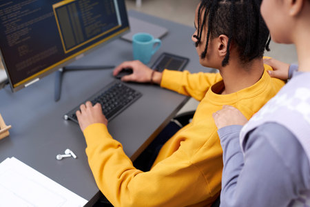 High angle view at two young people reviewing code together while working in IT development office and using compiterの写真素材