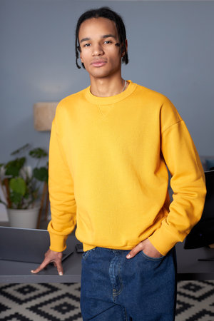 Vertical portrait of young black man wearing bright yellow hoodie while standing workplace and...