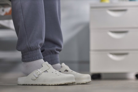 Close-up of patient in slippers and domestic clothes sitting on her bed in hospital wardの写真素材