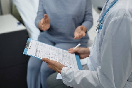 Close-up of doctor examining medical card of patient and talking to her during his visit in wardの写真素材
