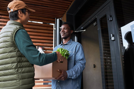 Waist up portrait of black young man accepting grocery delivery outdoors and smilingの写真素材