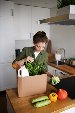 Vertical portrait of young woman unpacking fresh grocery delivery in kitchenの写真素材