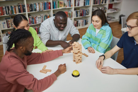 High angle view at diverse group of friends enjoying game of balance tower in library
