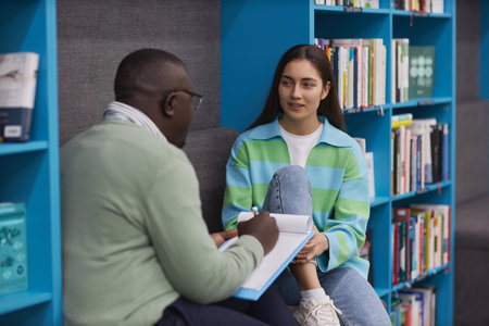 Portrait of young teenage girl talking to male therapist in college library and smilingの写真素材