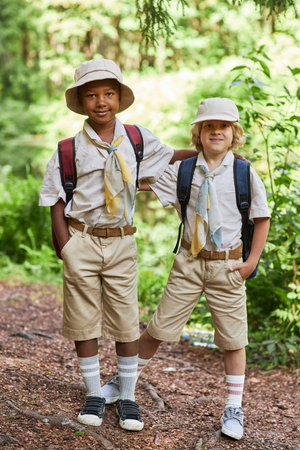 Vertical full length portrait of two cute boy scouts looking at camera outdoors in forest while...