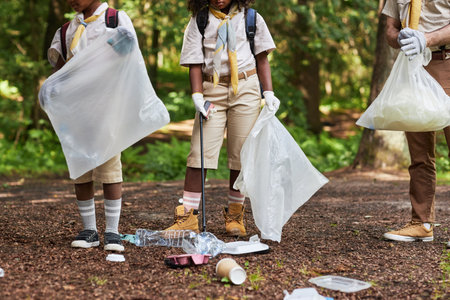 Low section of group of scouts picking up trash in forest during eco awareness field tripの写真素材