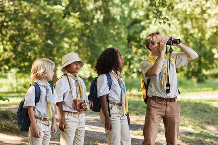 Group of scouts in forest exploring nature with adult scout leader looking in binocularsの写真素材