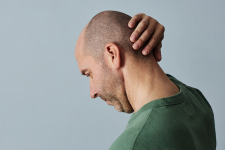 Minimal side view portrait of mature bald man touching head against pale grey background, copy spaceの写真素材