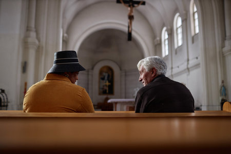 Rear view of senior people talking to each other while sitting on bench in old church during ministrationの写真素材