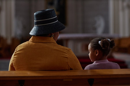 Rear view of African American grandmother sitting on bench with little girl during ministration in churchの写真素材