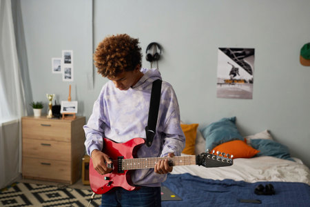 African American creative teenager in casualwear playing electric guitar while standing in front of...