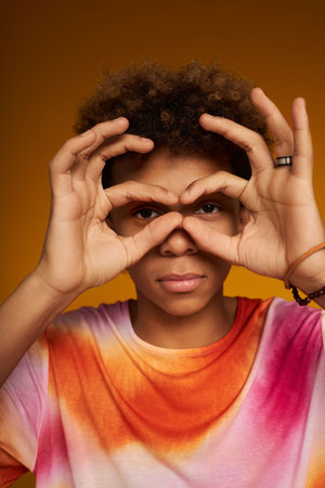 Close-up of teenage boy looking at camera keeping hands by his eyes during photo shooting against...